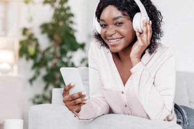 Dijital Müzik Servisi. Kablosuz kulaklıklar takan, akıllı telefondan favori şarkıları dinleyen, evdeki koltukta dinlenen, yakın plan