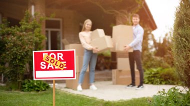 Taşındıkları gün yeni evlerinin önünde kutuları olan genç çift, satış tabelasına odaklanıyor. Boşluğu kopyala