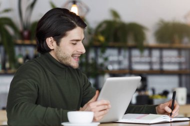 Gülümseyen adam kafede yeni bir proje üzerinde çalışıyor, dijital tablet kullanıyor, boşluğu kopyalıyor