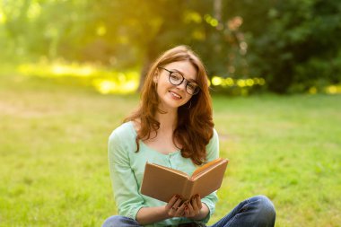 Temiz hava üzerinde çalışıyorum. Neşeli kızıl saçlı kız elinde kitapla çimlerde oturuyor, sınavlara hazırlanıyor ya da okuyor.