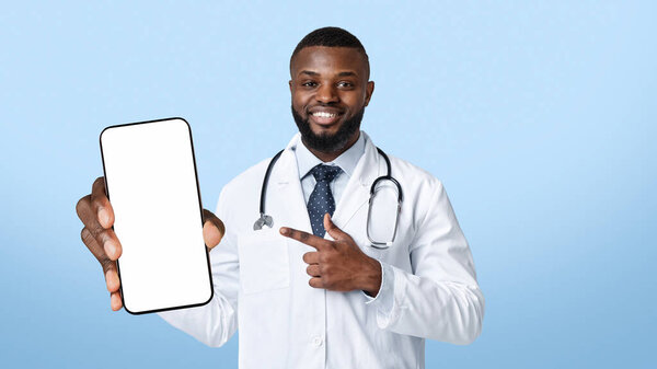 Улыбающийся черный врач со стетоскопом, указывающий на мобильный телефон с пустым экраном, копирующее пространство