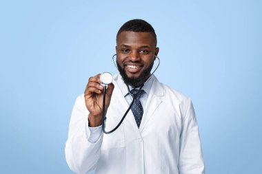 Afrikalı neşeli terapistin portresi. Steteskopla hastanın akciğerlerini kontrol ediyor. Beyaz stüdyo geçmişi var.