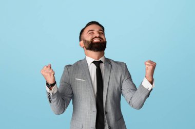 Zafer ve başarı. Yakışıklı işadamı heyecanlı ve mavi arka planda EVET işareti yapıyor