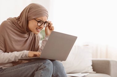 Görme sorunu. Başörtülü Müslüman Kadın dizüstü bilgisayara bakarken gözlerini kısarak bakıyor, görüş sorunu yaşıyor, Boşluğu Kopyala