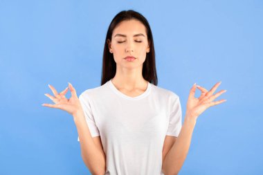 - Sakin ol. Huzurlu genç kadın yoga alıştırması yapıyor gözleri kapalı, mavi stüdyo duvarı