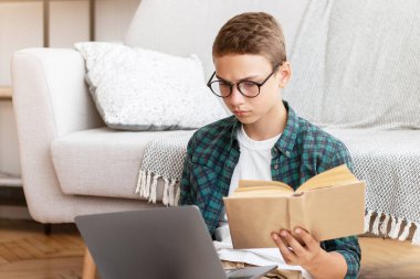 Akıllı okul çocuğu kompozisyon yazıyor, kitap tutuyor ve dizüstü bilgisayarda daktilo yazıyor, evde çalışıyor.