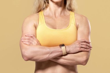 Sağlıklı bir yaşam tarzı, formda kalmak, güzel bir vücut. Spor giyim sektöründe kendine güvenen, spor kıyafetli çekici bir kadın ellerini çapraz yapmış, kameraya bakın, bej arka planda izole edilmiş, stüdyo çekimi, panorama.