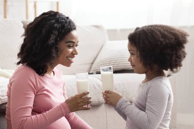Sağlıklı içecek. Küçük afro kız ve hamile annesi evde oturmuş süt içiyorlar, birbirlerine bağlanıyorlar..