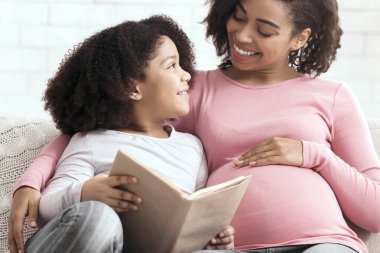 Educational Activities. Happy African Mom And Her Little Daughter Reading Book Together, Sitting On Couch In Living Room At Home, Free Space