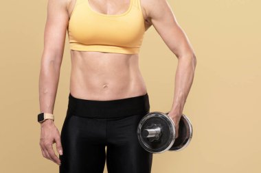 Formda kal, spor yap ve kendini izole etme eğitimi al. Ev ya da spor salonunda kapalı tut. Dambıl egzersizi yapan orta yaşlı kaslı kadın, bej arka planda izole edilmiş.