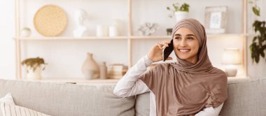 Memnun oldum. Modern Müslüman kız evde cep telefonuyla konuşuyor ve uzaklara bakıyor, kopya alanı olan panorama