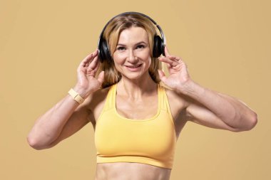 Müzikle çalışmak, covid-19 'dan kendini soyutlama sırasında aktif boş zaman. Spor üniformalı, kulaklık takan, spor yapan, dans eden, bej arka planda izole edilmiş, boş bir alanda yaşayan mutlu, kaslı bir kadın.