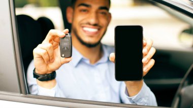 Neşeli orta doğulu işadamı güzel bir otomobilin içinde oturuyor, araba anahtarı ve akıllı telefonu boş ekran ile gösteriyor, olumlu Arap adam araba kiralama, taklit, kopyalama için çevrimiçi servis öneriyor.