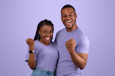 Vay canına, evet. Aşırı neşeli genç zenci erkek ve kadının portresi. Sarılma ve sıkılmış yumrukları sallama, tezahürat ve kameraya bakma. Heyecanlı çift mor arkaplan duvarının üzerinde dikiliyor.