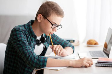 Akıllı bir öğrenci ödevlerini çok sıkı yapıyor, evde masa başında oturuyor ve kompozisyon yazıyor, online eğitim kavramı.