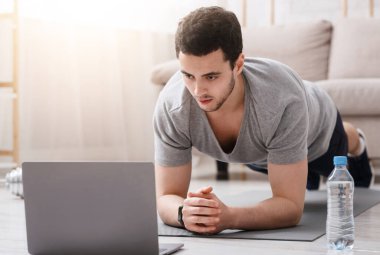 Evden çalış ve çalış. Evdeki oturma odasının iç tarafında dizüstü bilgisayar ve su döşeyen genç bir adam.