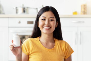 Gülümseyen genç Çinli bayan mutfak zemininde şirin uzun paltolu köpek Jack russel terrier ile oturuyor, evcil hayvanlar için takviye veya vitamin içeren beyaz kavanozu gösteriyor,