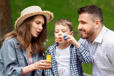 Oğulları parkta piknik yaparken sabun köpüğü üflediği için mutlu genç ebeveynler.