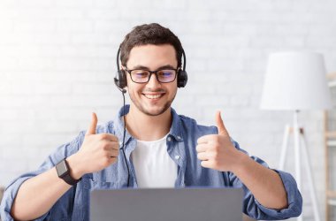 Çevrimiçi iş ve modern blog. Kulaklık takan gülümseyen adam evde dizüstü bilgisayarla harika bir işaret veriyor.