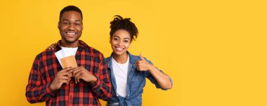 Tatil Seyahat Konsepti. Mutlu Afrikalı Turistler Uçuş Biletleri Tutan Çift Sarı Stüdyo Arkaplanında Başparmak Pozu Veriyor. Seyahat, Turizm ve Tatil Gezisi. Panorama