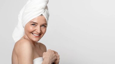 Spa 'dan sonra. Kafasında havluyla kameraya gülümseyen, güzellik tedavisinden sonra banyoda poz veren mutlu olgun bir kadının portresi.