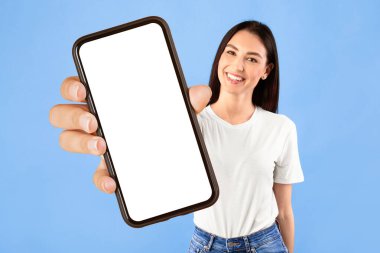 Mavi arka planda izole bir şekilde duran mutlu genç bayan portresi, sizi işaret ederken kameraya bakıyor.