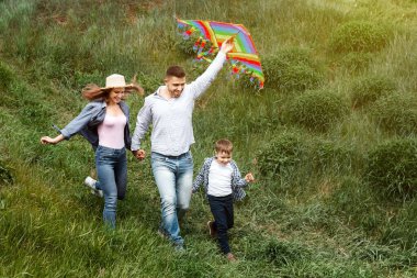 Yaz aile aktiviteleri. Oğullarıyla kırsalda uçurtma uçuran neşeli genç ebeveynler.