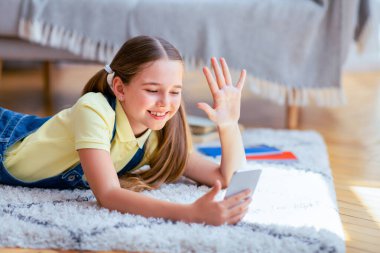 Hoş geldiniz. Cep telefonuyla video görüşmesi yapan, kameraya el sallayan, halıya uzanan, uzayı kopyalayan tatlı bir kız.