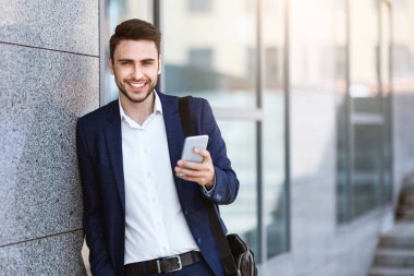 Akıllı telefonlu bir şirket çalışanı şehir caddesinde ofis kulesinin yanında duruyor.