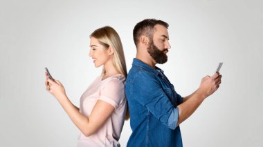 Evli bir çift sırt sırta durur, her biri akıllı telefonlarına dalmıştır. Yakın çevresine rağmen kopuk görünüyorlar, modern ilişkilerin zorluklarını gösteriyorlar..