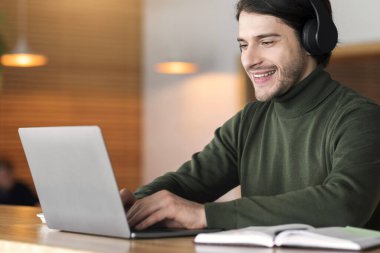 Kablosuz kulaklıklı genç adam kafede dizüstü bilgisayarda çalışıyor, eğitim online konsept, boş alan