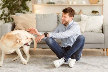 - Boş zaman. Yakışıklı bir adam oturma odasında köpeğiyle oynuyor, yerde oturuyor.