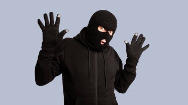 Eller yukarı! Maskeli soyguncu polis tarafından tutuklandı, beyaz stüdyo arka planında yalnız poz verdi ve durdu.