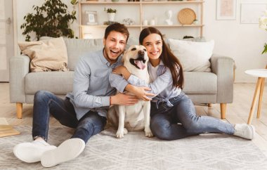 Mutlu Aile Kavramı. Modern apartmanda yerde oturan köpekli güzel bir çiftin portresi.