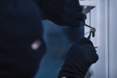 Ev soygunu sırasında siyah maskeli soyguncunun kapı kilidini metal maymuncukla açması.