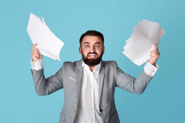 İş stresi ile başa çıkmak. Öfkeli çok çalışan ofis çalışanı mavi arka planda kağıt dökümanları tutuyor.