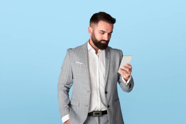 Millennial ofis çalışanı mavi arka planda akıllı telefondan iletişim kuruyor.