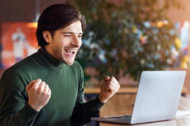 Duygusal adam dizüstü bilgisayara bakıyor, yumruklarını sıkıyor ve bağırıyor, iyi haberler var, boş alan.