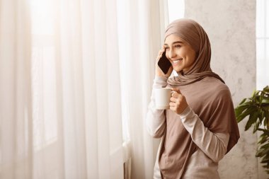 Rahatlamış bir hafta sonu. Başörtülü, gülümseyen, kahve içen ve cep telefonuyla konuşan Müslüman kadın.