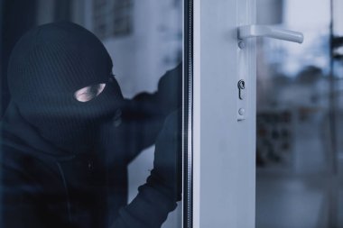 Siyah kar maskeli soyguncunun portresi. Ev soygunu sırasında cam kapı kilidi. Evin içinden görüntü.