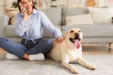Günlük Yaşam Konsepti. Sıradan bir kız cep telefonuyla konuşuyor, Labrador 'u okşuyor, oturma odasında yerde oturuyor.