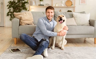 Sen benim en iyi arkadaşımsın. Modern bir dairede köpeğini kucaklayan yakışıklı bir adamın portresi.