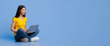 Gülümseyen Asyalı genç bir kadın dizüstü bilgisayarla mor stüdyo arka planında oturuyor, fotokopi alanına bakıyor, bin yıllık Koreli kadın not defteriyle çalışıyor ya da çalışıyor.