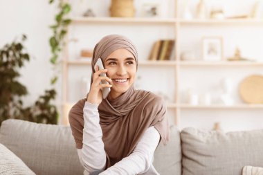 Uzun zamandır beklenen arama. Mutlu Müslüman kız tesettürde telefonla konuşuyor, cep telefonuyla konuşuyor ve gülümsüyor.