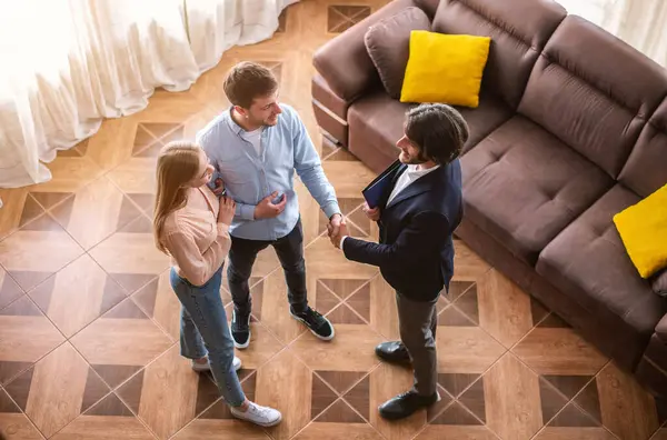 Mutlu evli çift ve emlakçı ev içi emlak anlaşması yaptıktan sonra el sıkışıyor.