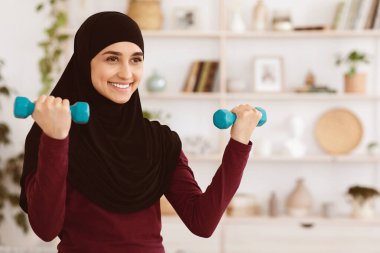 Ev antrenmanı. Oturma odasında dambıllı güçlü genç kadın eğitimi, kapalı alanda spor aktiviteleri, boş alan.