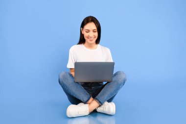 Serbest çalışmak ya da İçişleri Bakanlığı. Güzel bir kadın yerde oturuyor ve bacak bacak üstüne atmış taşınabilir bilgisayar kullanıyor.