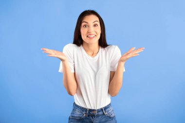 Kim bilir. Pozitif Genç Kadın Omuz silkme portresi Mavi Arkaplanda Gülümseyen Kamera Pozisyonu. Stüdyo çekimi. Kafası karışık bayan hiçbir şey bilmiyor. Özür dilerim, izninizle. Karar veremiyorum.