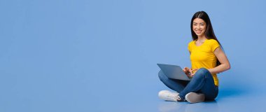 Milenyum Asyalı Kız dizüstü bilgisayarla yerde oturuyor, Mor arkaplanda uzaktan çalışıyor, Boş Alanlı Panorama