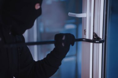 Vandalizm Konsepti. Siyah kar maskesi ve eldiven giyen davetsiz misafirin levyeyle ev kapısını kırması.